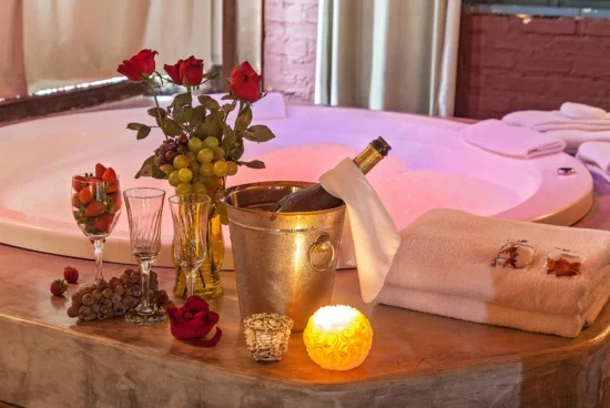 Hidromassagem do Loft da Serra com decoração romântica, rosas vermelhas, frutas, taças, champanhe e toalhas sobre a bancada.