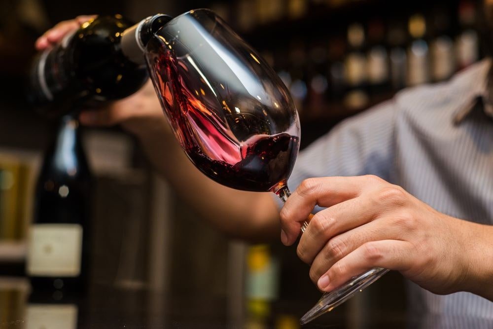 Garçom enchendo uma taça de vinho tinto com ambiente do retaurante desfocado ao fundo